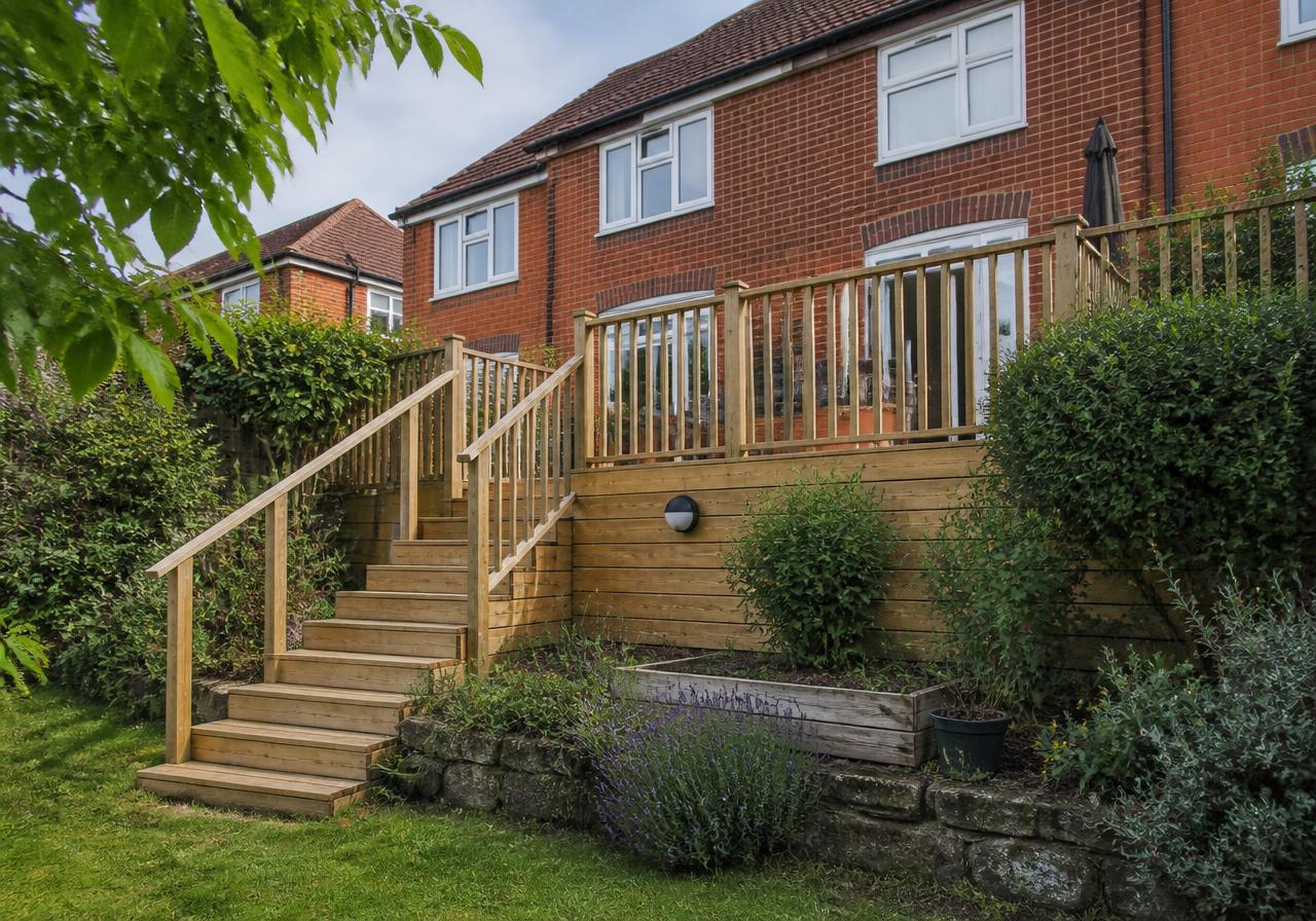 Raised timber decking with steps and handrail against a red brick Cheshire house